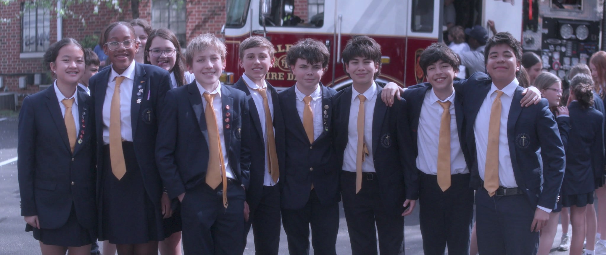 Students in navy blazers and gold ties standing together outside